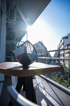 Un balcon avec une table, un fauteuil suspendu et une vue sur les bâtiments en arrière-plan.