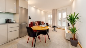 A modern kitchen with a refrigerator, a dining table with chairs, a red sofa, and a potted plant. - High Classe One Bedroom Apt for 3 - River View 3 (Vila Nova de Gaia)