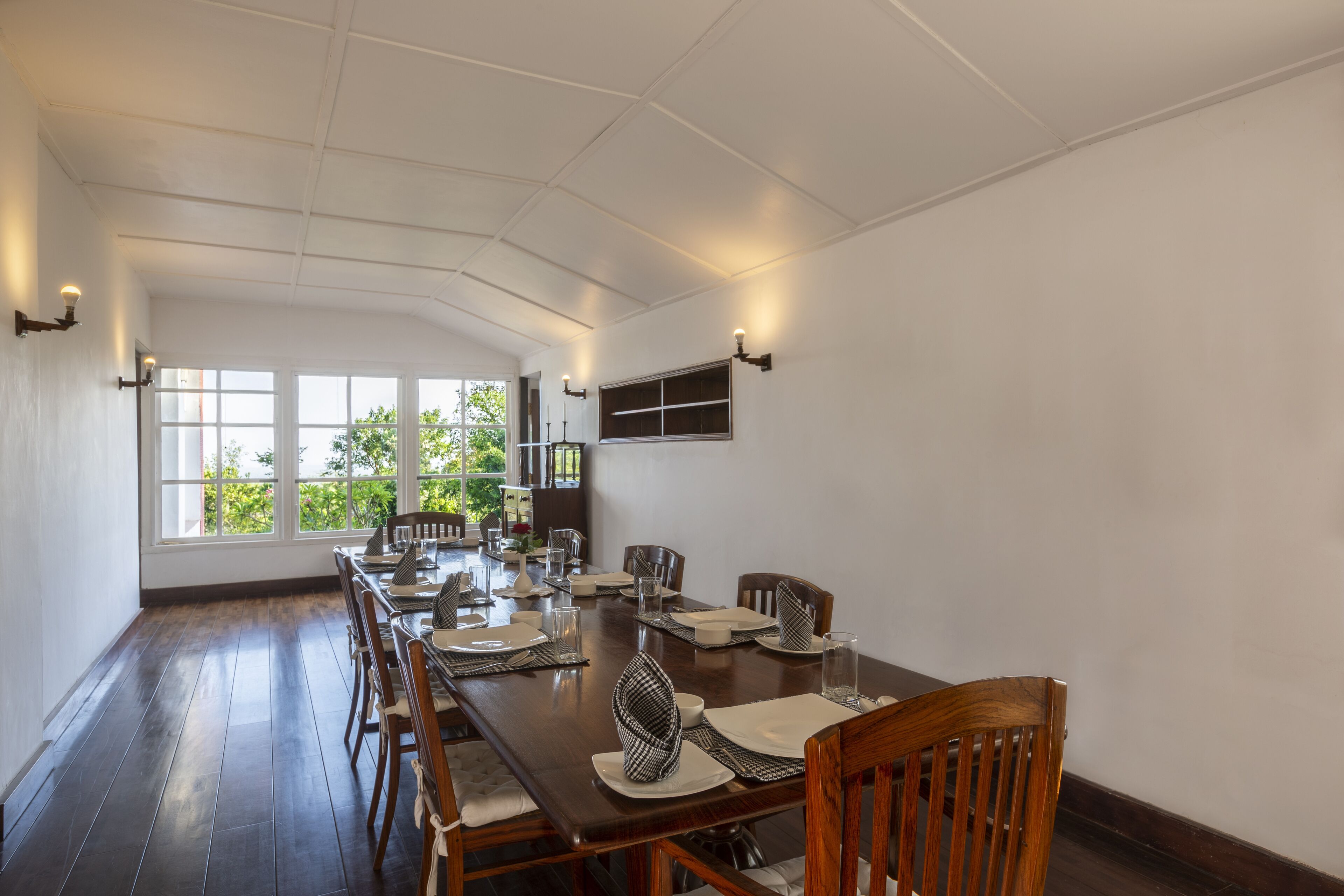 Comedor con una larga mesa dispuesta para una comida, ventanas amplias y vistas a la vegetación exterior.
