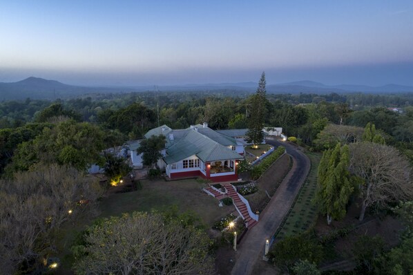 A large house with a red and white exterior, surrounded by lush greenery and a winding driveway.