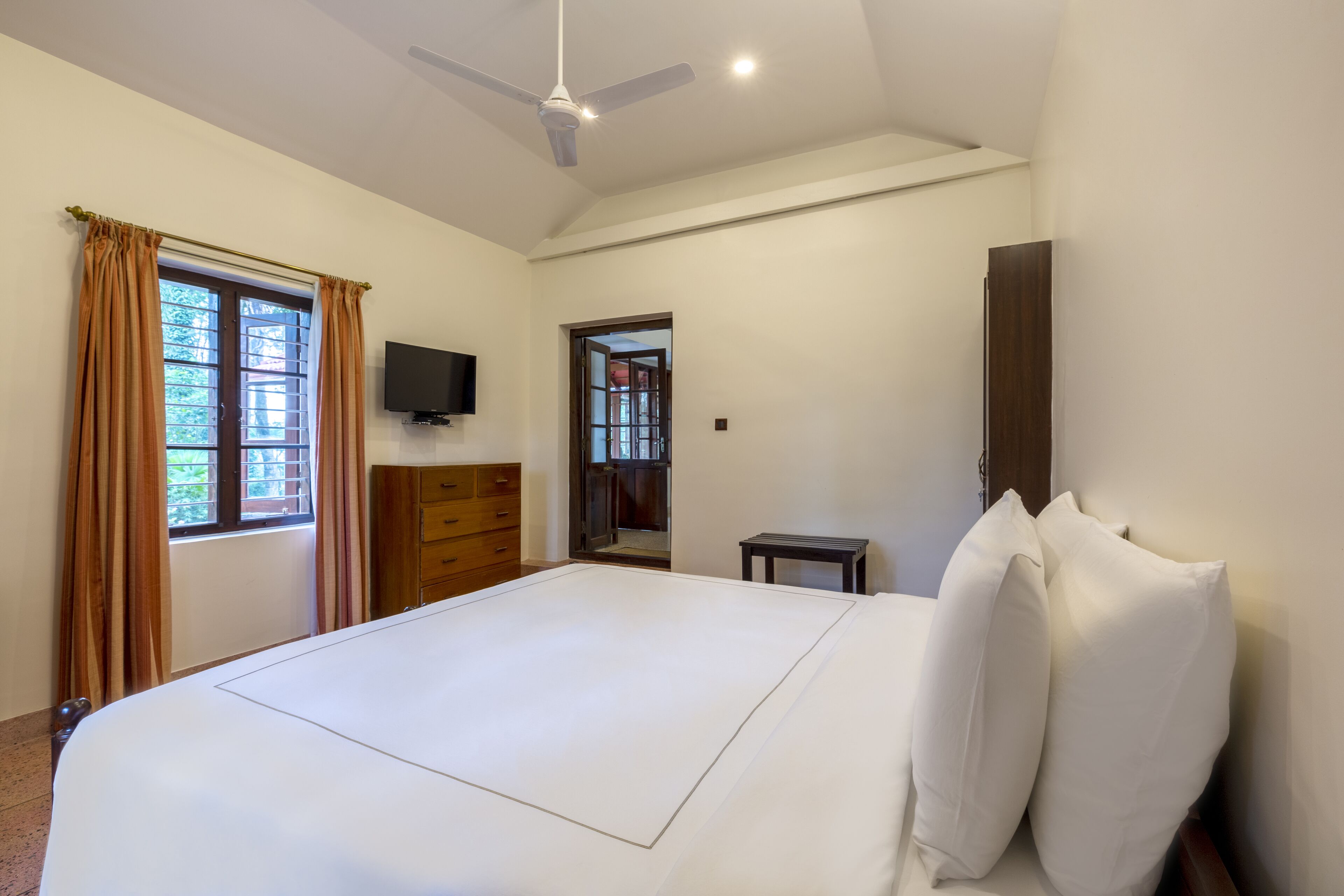 A hotel room with a large bed, a ceiling fan, a TV, and a wardrobe.