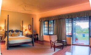 A four-poster bed with a headboard, a chair, a table, and a window with curtains.
