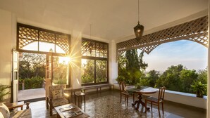 Un patio amplio con mesa, sillas y sofá. Ventanas grandes ofrecen vista al follaje circundante.