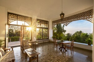 Un patio amplio con mesa, sillas y sofá. Ventanas grandes ofrecen vista al follaje circundante.