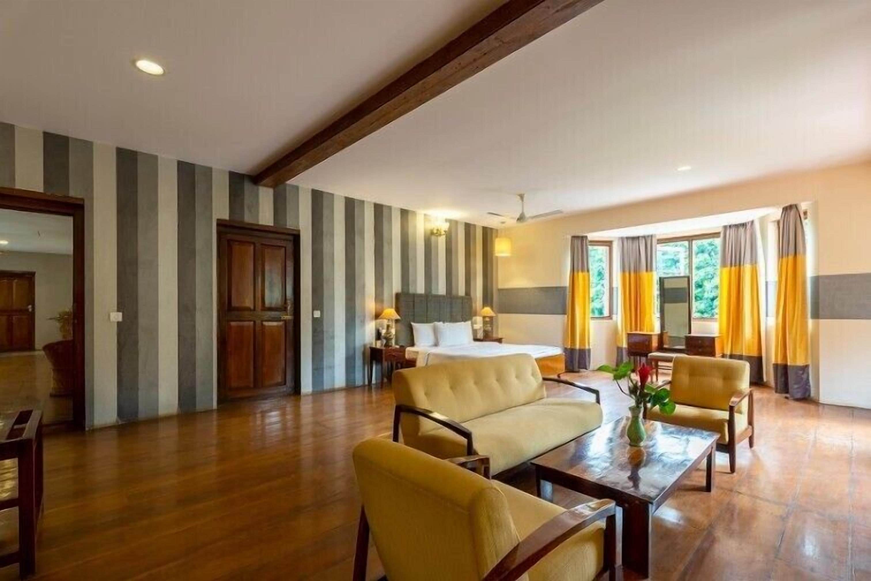 A hotel room with a bed, a sofa, a dining table, and a window with curtains.