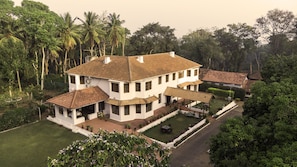 A large, two-story house with a tiled roof, surrounded by lush greenery and palm trees.