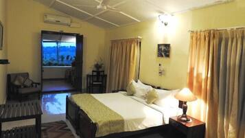 Una habitación de hotel con cama, lámpara de noche, ventana con cortinas, una silla y vistas al exterior.