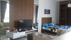 A modern hotel room with a flat-screen TV, a sofa, a bed with colorful bedding, a wardrobe, and a painting on the wall. - Studio At Mansion One (George Town)