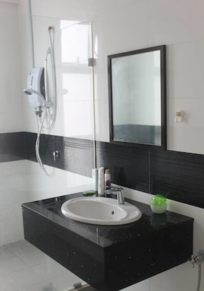 A modern bathroom with a black and white tiled wall, a white sink, and a glass shower enclosure. - Studio At Mansion One (George Town)