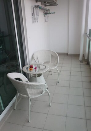 A balcony with two white wicker chairs and a small round table with a flower vase. - Studio At Mansion One (George Town)