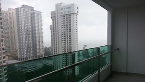 A balcony with a glass railing overlooking high-rise buildings. - Studio At Mansion One (George Town)