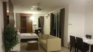 A hotel room with a bed, a sofa, a dining table with chairs, and a potted plant. - Studio At Mansion One (George Town)