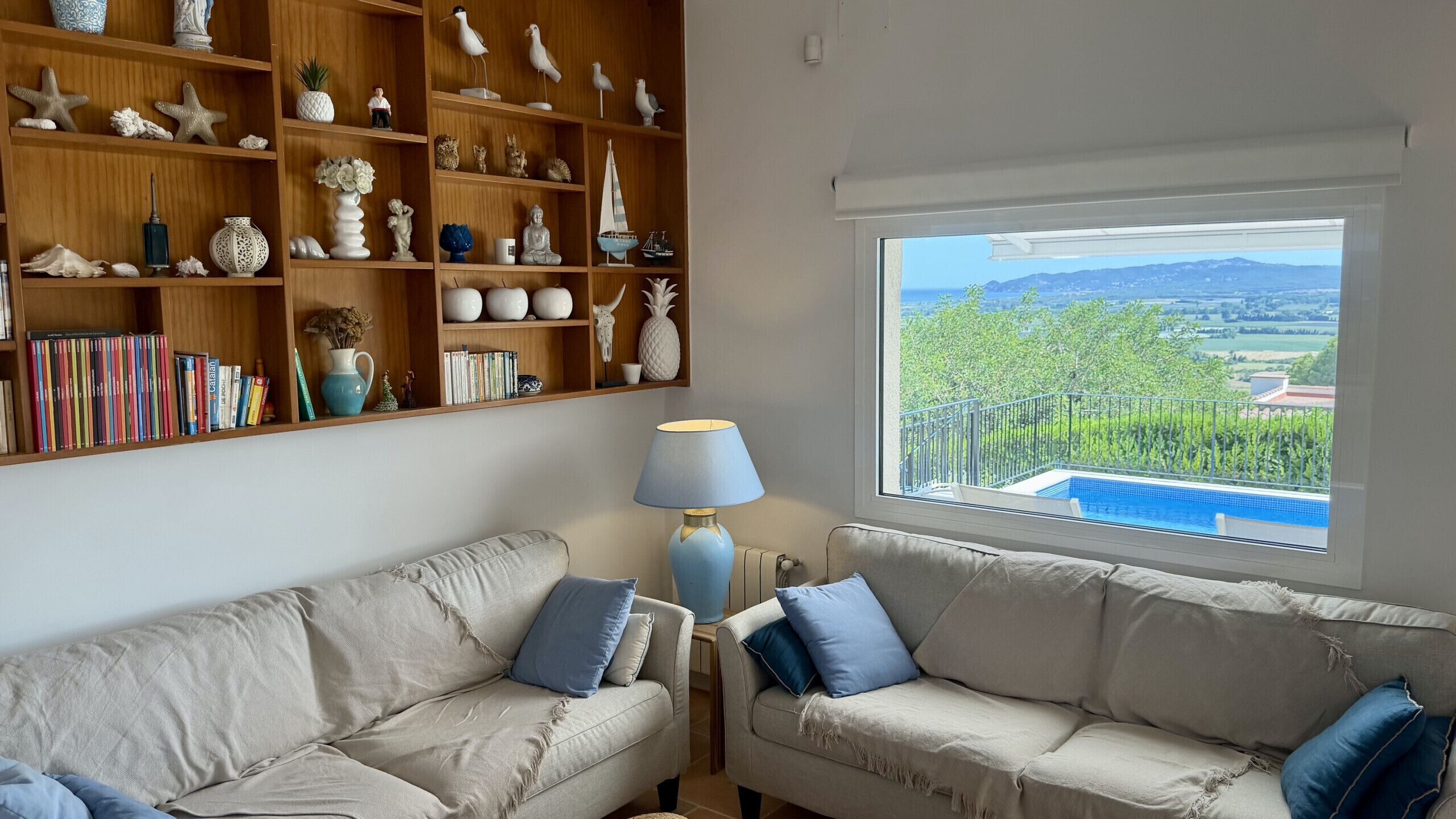 Una sala de estar con dos sofás, una estantería y vista a una piscina.