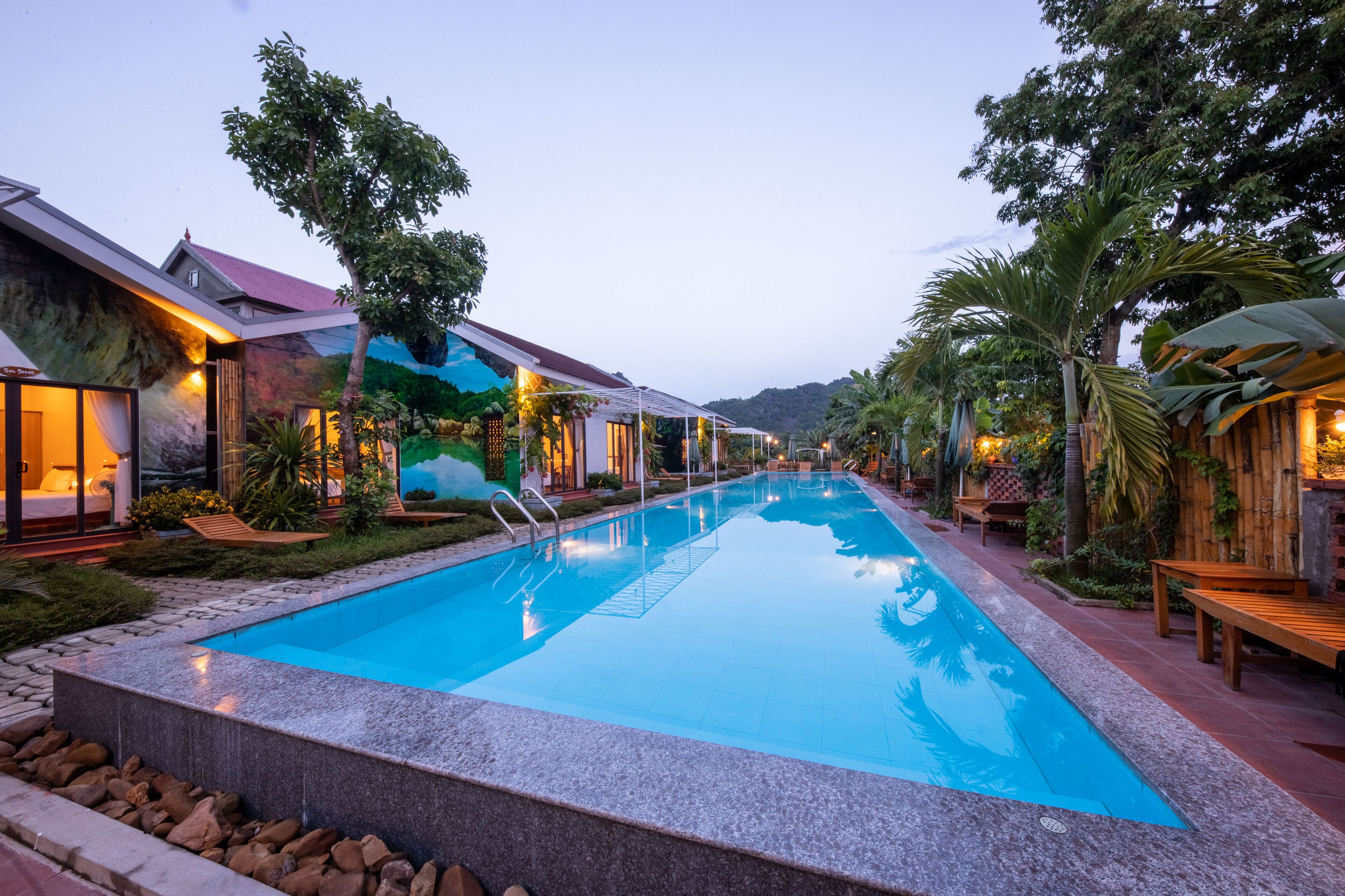 A swimming pool with a stone border, surrounded by wooden benches and tropical plants.