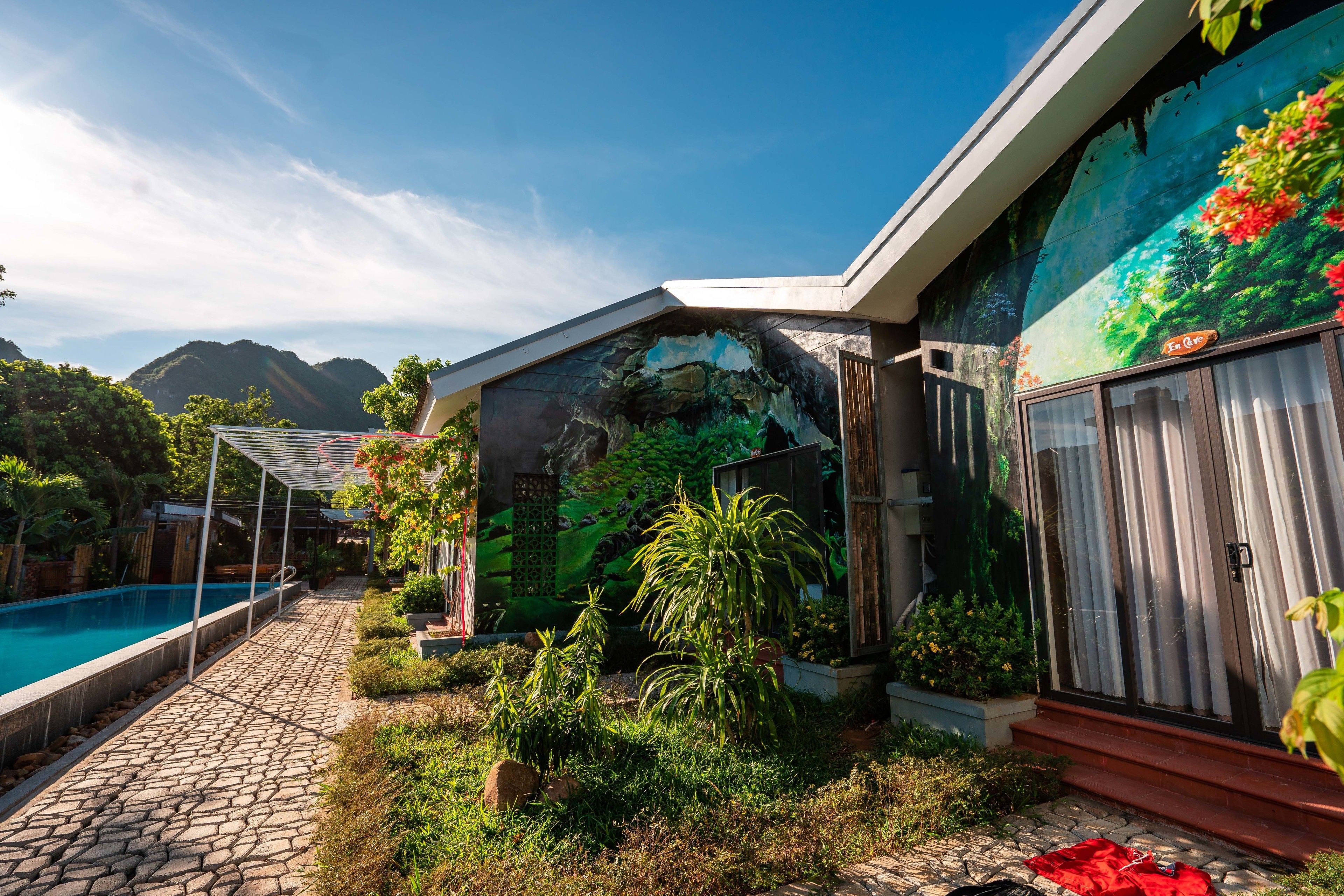 Ein Haus mit Swimmingpool, ein Garten mit verschiedenen Pflanzen und einem Wandgemälde an der Seite.