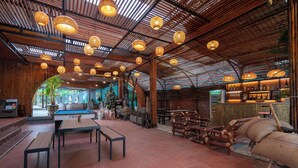 A spacious indoor area with wooden beams and hanging lights, featuring a pool table, seating areas, and a bar. - Commander Lodge (Phong Nha)