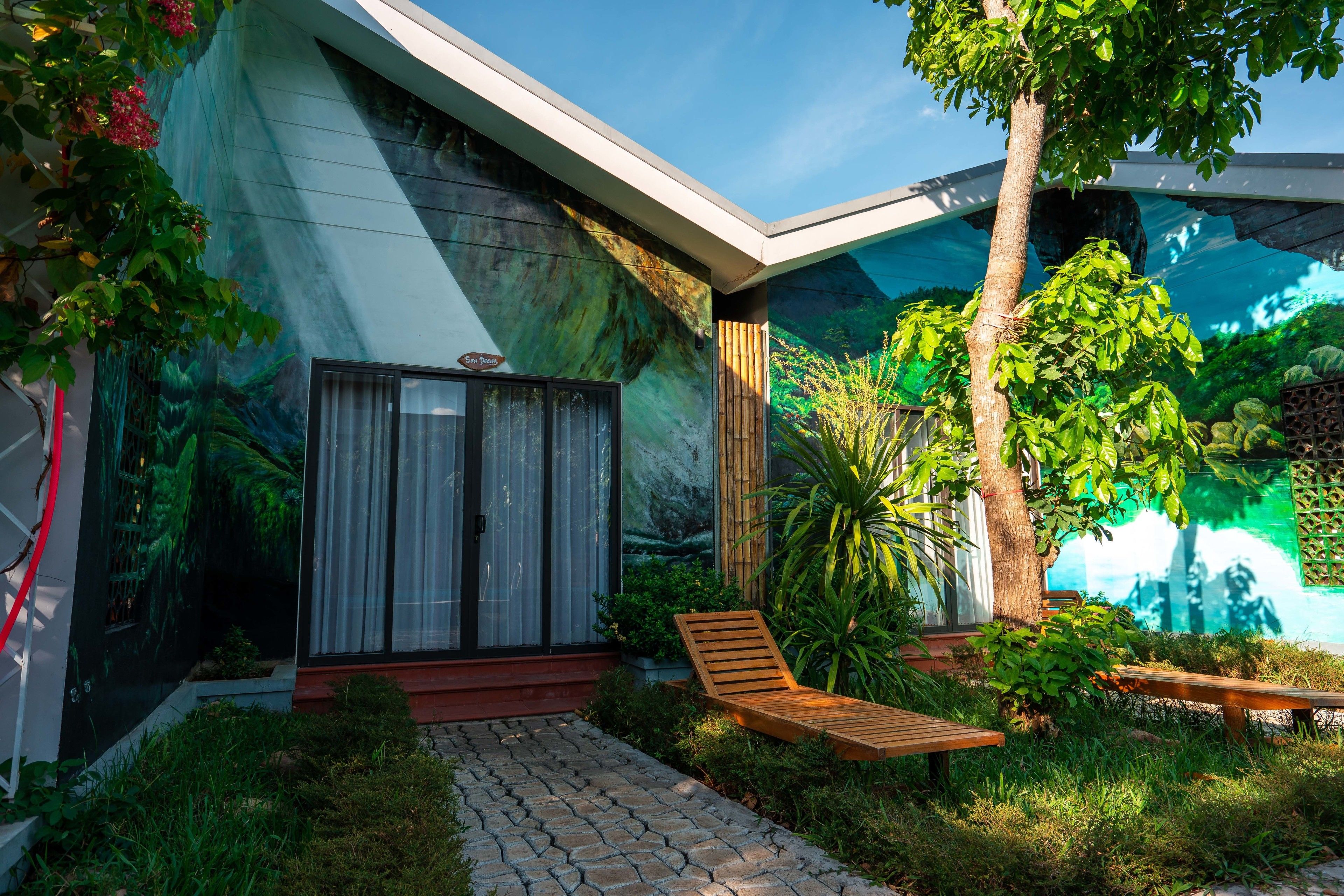 A modern house with a stone pathway leading to a wooden bench and a glass door.
