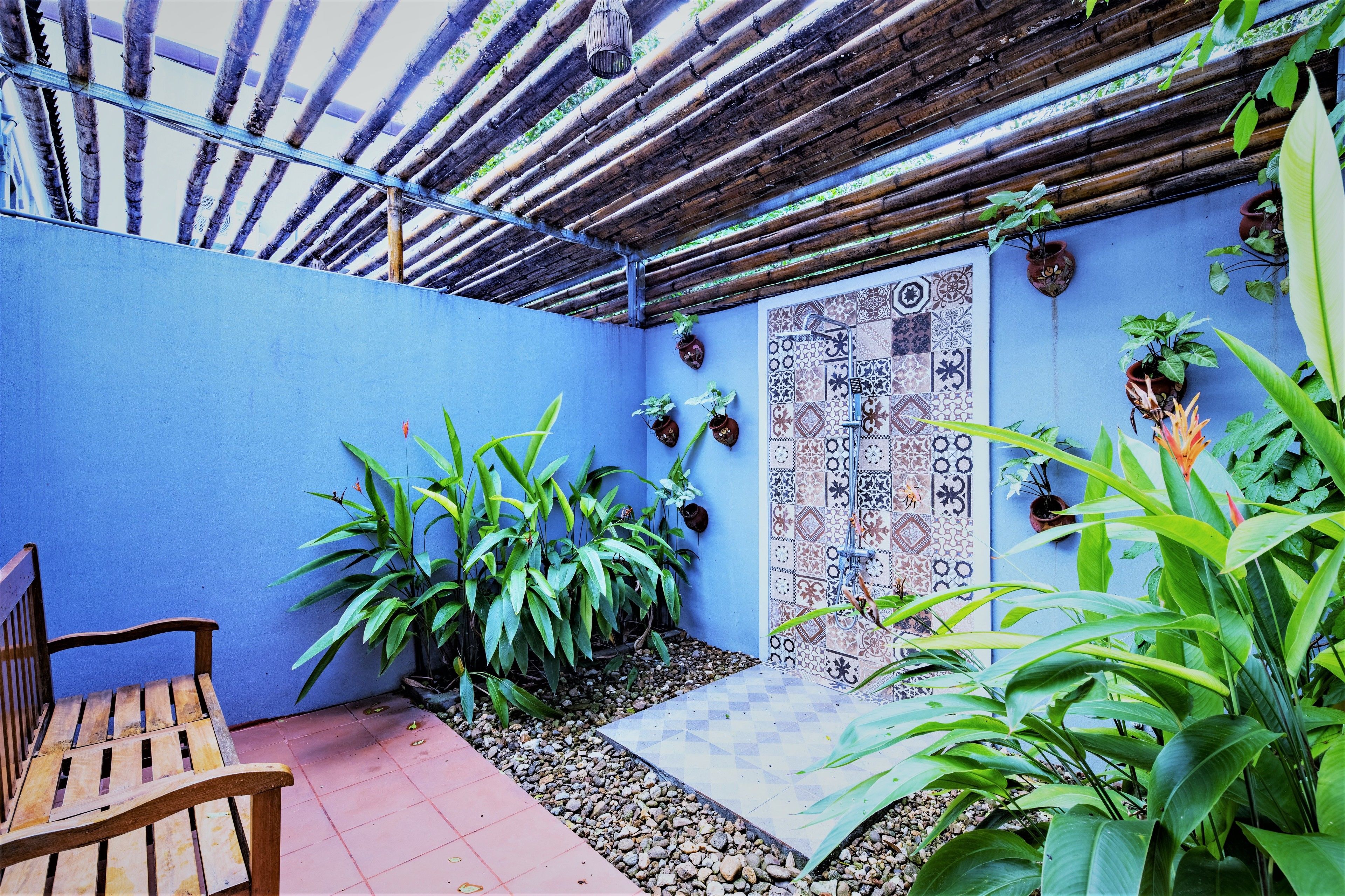 A small patio area with a wooden bench, potted plants, and a tiled wall with a geometric pattern.