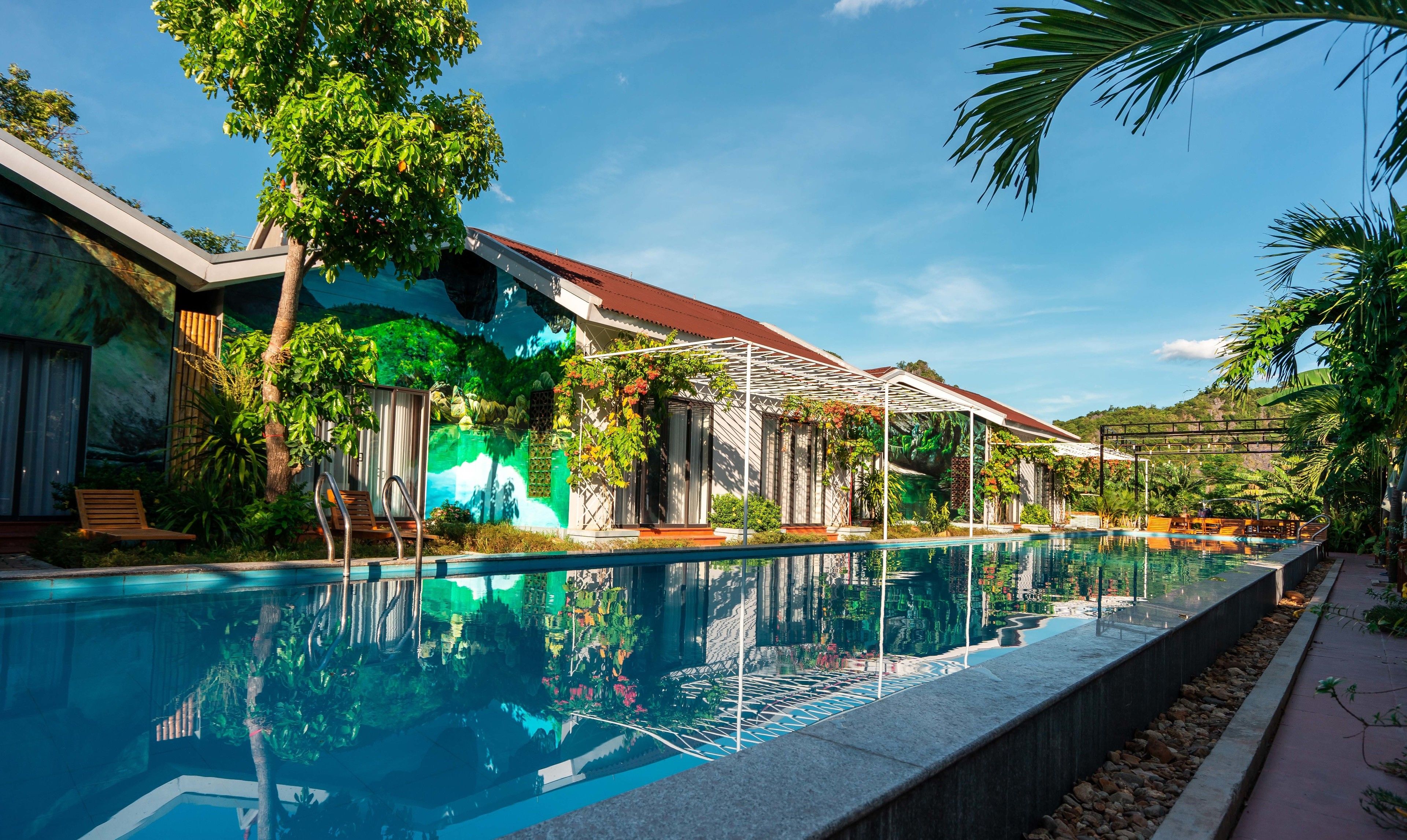A swimming pool with a clear view of the surrounding architecture, including a building with a red roof and a covered patio area.