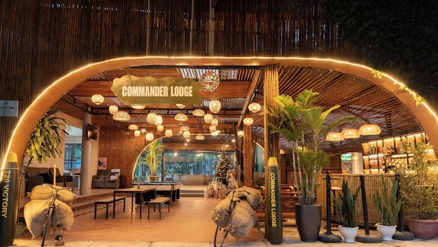 A cozy lobby with a wooden archway labeled "Commander Lodge," featuring hanging lights, comfortable seating, and potted plants. - Commander Lodge (Phong Nha)