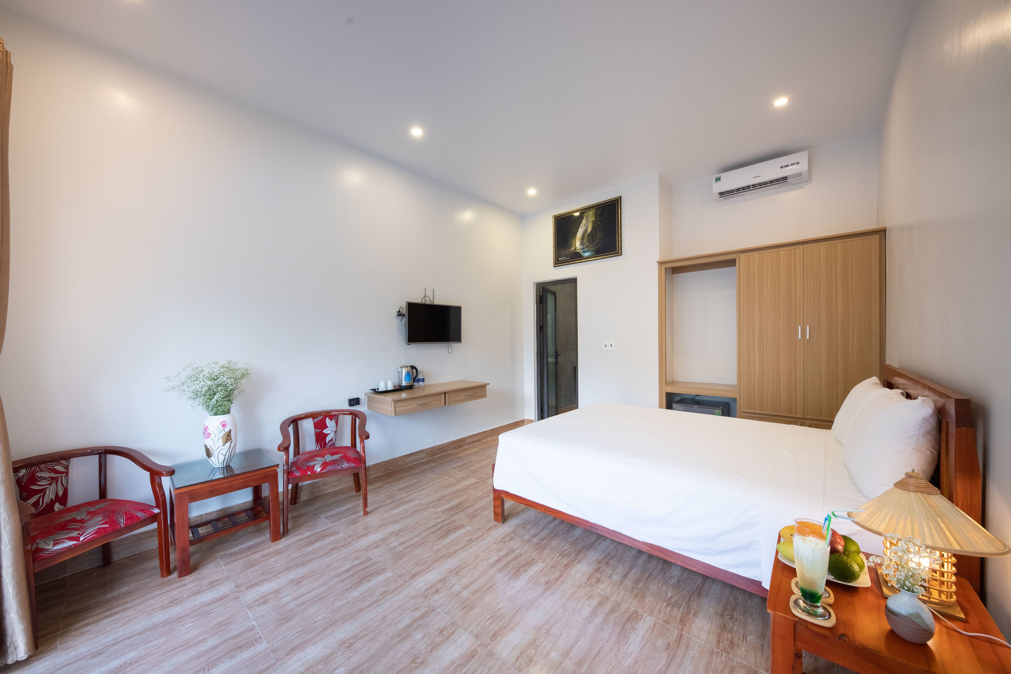 Habitación de hotel con cama, escritorio con silla, televisor, armario y mesita de noche con lámpara y frutero.