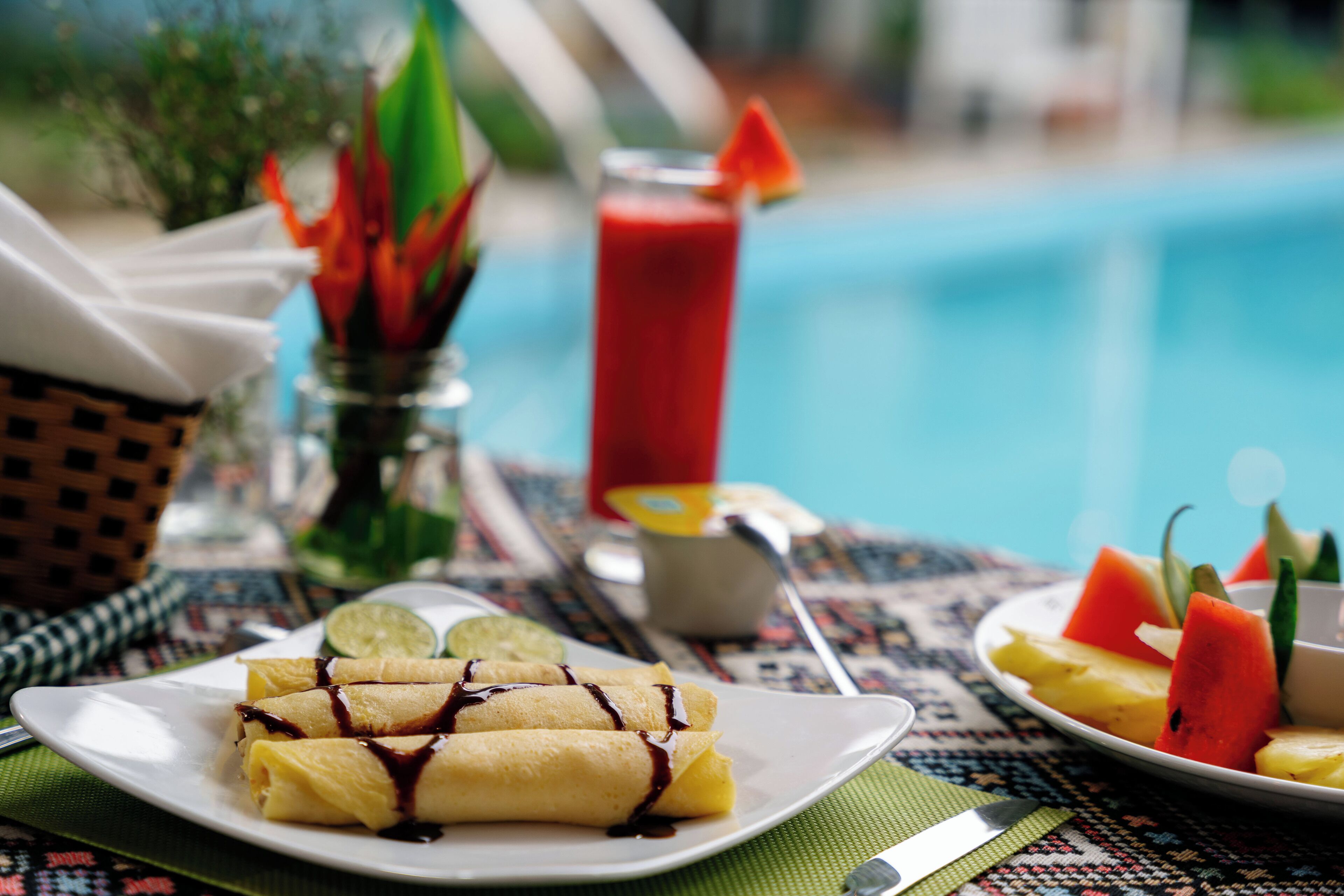 Une table à manger avec une assiette de crêpes, un verre de boisson rouge et une assiette de fruits.