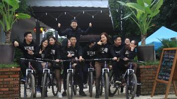 A group of people on bicycles in front of a building with a brick wall and a signboard.