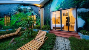 A modern hotel with a glass facade, a lush garden, and a mural of a forest scene. - Commander Lodge (Phong Nha)