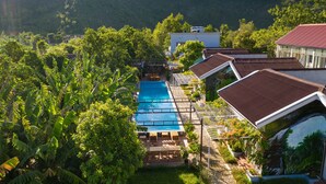 A resort with a swimming pool, lush greenery, and mountainous views. - Commander Lodge (Phong Nha)