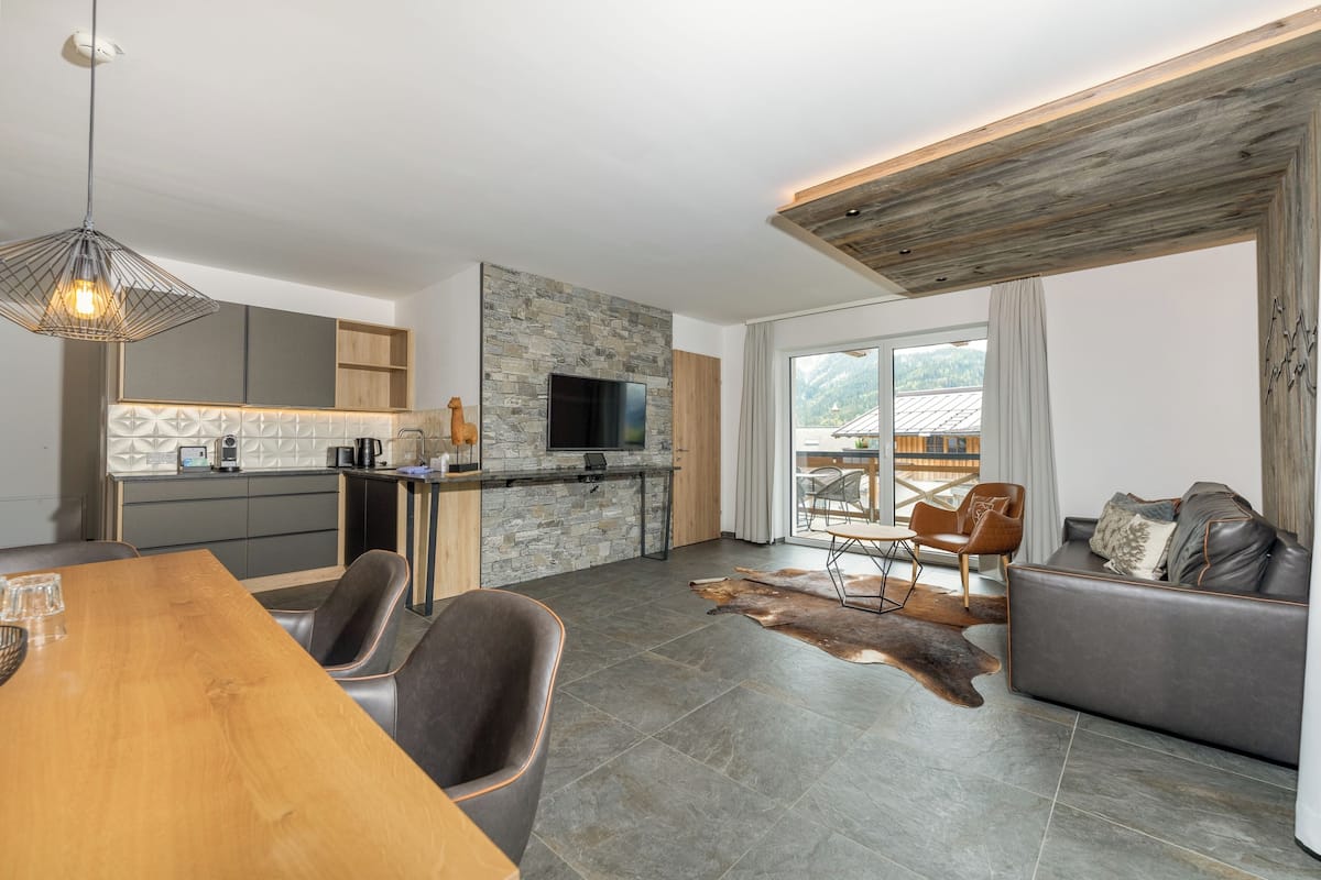 Eine moderne Küche mit Steinrückwand, einem Flachbildfernseher und einem Essbereich mit Holztisch und Ledersesseln.