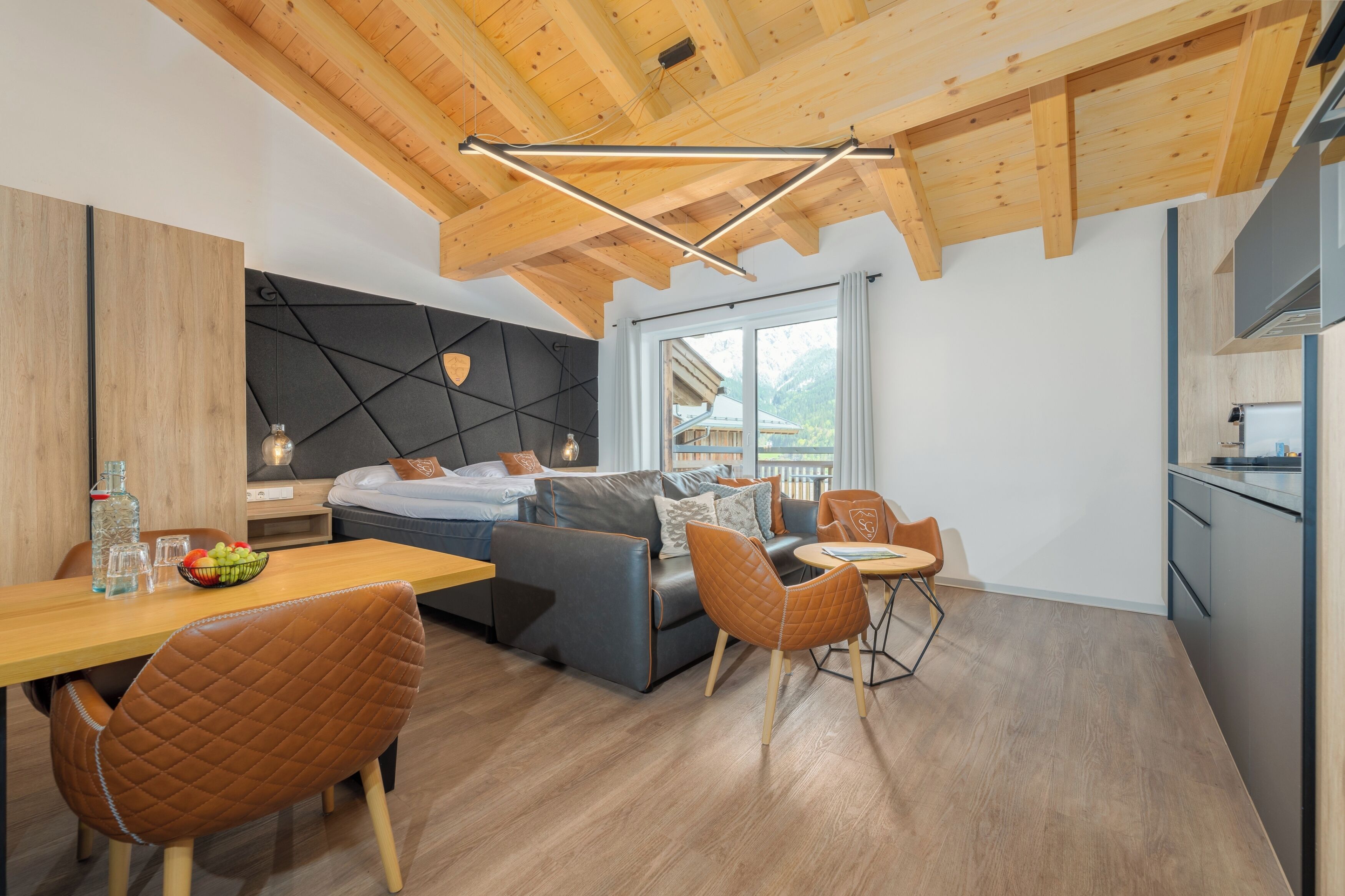 A modern room with a wooden ceiling, a sofa, a dining table, and a kitchen area.
