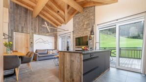 Une cuisine moderne dotée d’un îlot central en bois, d’un pare-feu en pierre et de grandes fenêtres offrant une vue sur un paysage verdoyant.