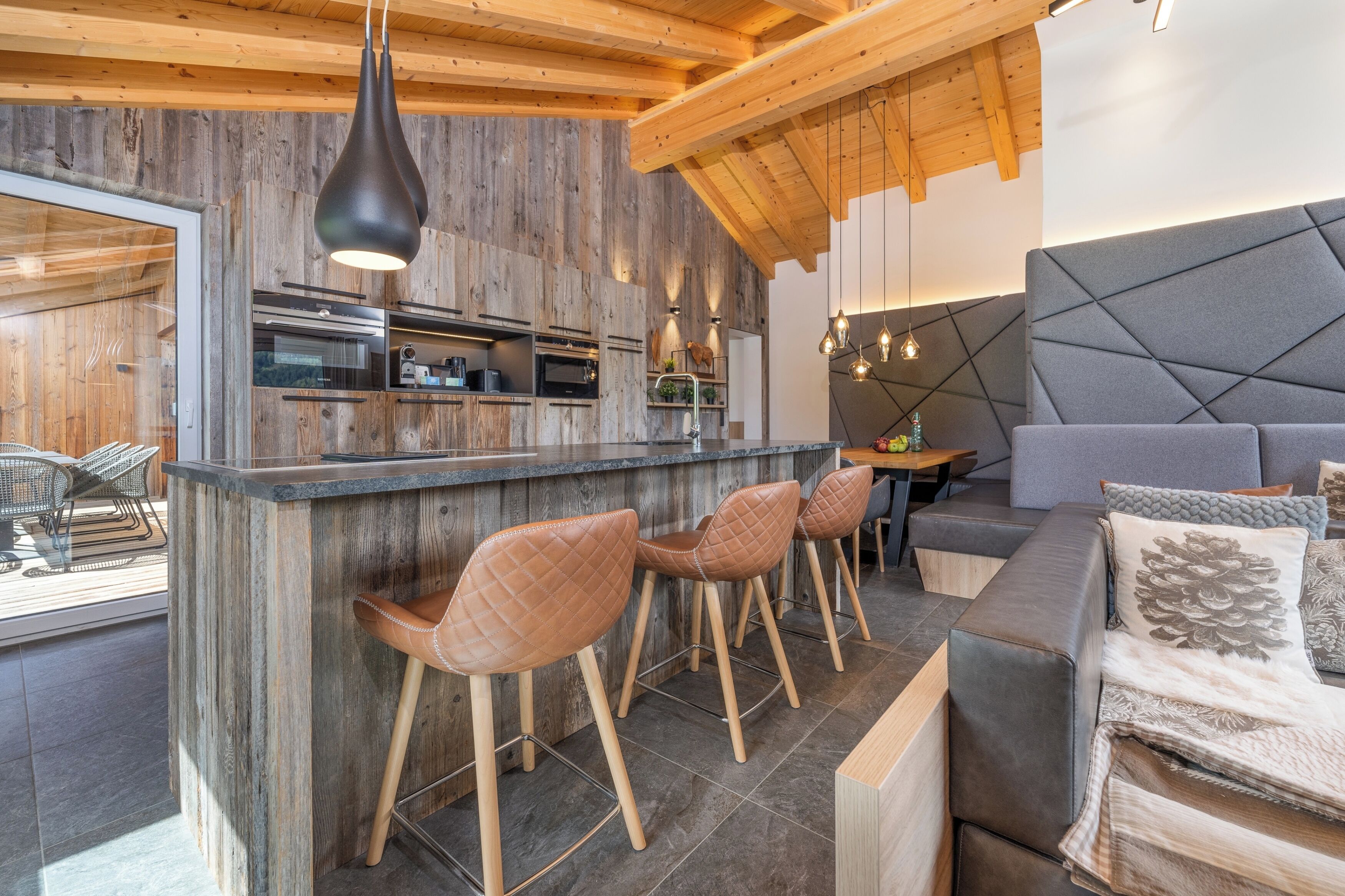 Una cocina moderna con detalles de madera, una zona de bar con taburetes y un rincón de estar acogedor con cojines.