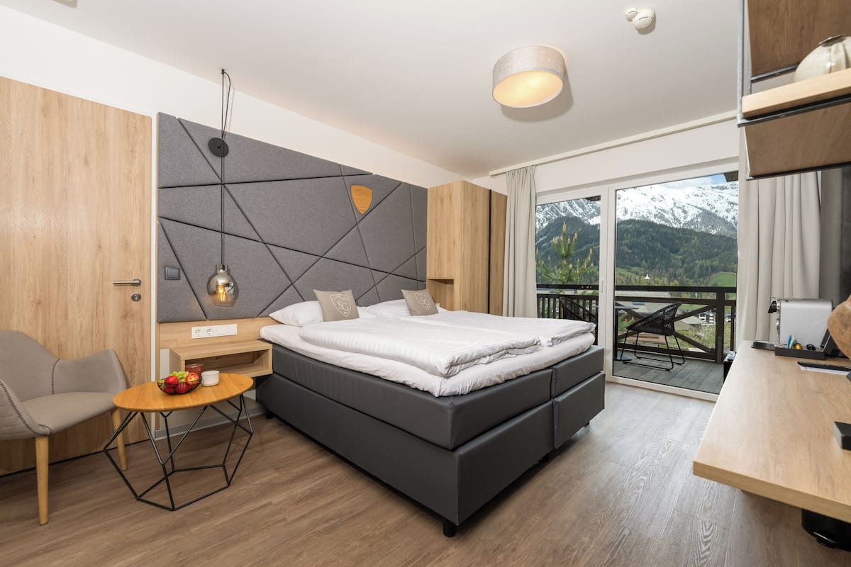 Ein modernes Schlafzimmer mit einem großen Bett, einem Holztisch, einem Stuhl und einem Balkon mit Blick auf die Berge.