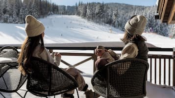 Two people sitting on outdoor chairs facing a snowy ski slope.