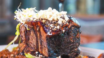 A steak with sprouts and a sauce on a plate, with a glass of red wine in the background.