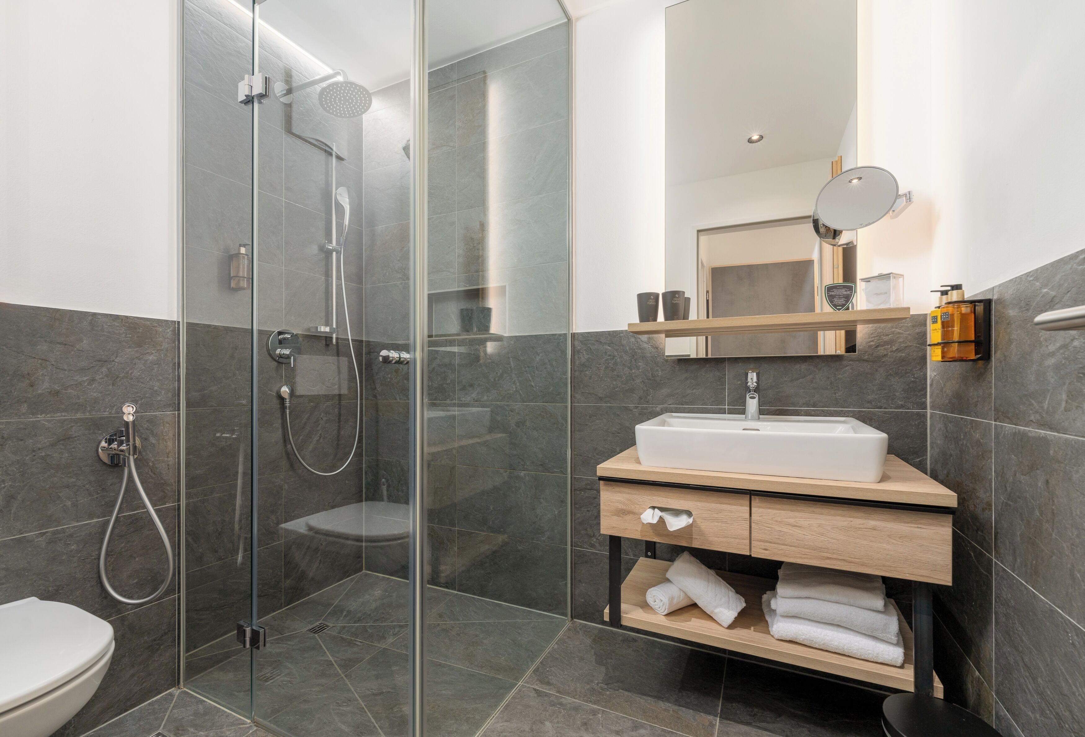 A modern bathroom with a glass-enclosed shower, a white sink, and a wooden vanity.