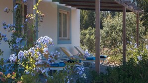 Un espace extérieur aménagé, abrité et doté de chaises longues et d’une pergola, entouré d’une végétation luxuriante et de plantes en fleurs.