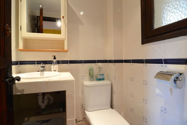 A bathroom with a white sink, toilet, and mirror. There is a shelf above the sink and a towel rack to the right. - PASSATGE BERNA, 2 (Estartit)