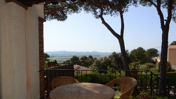 Um terraço com móveis de vime, uma mesa e vista para colinas e árvores ao longe.