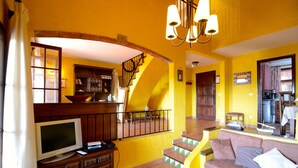 Uma sala de estar com televisão, móveis de madeira, uma escada e uma parede amarela.