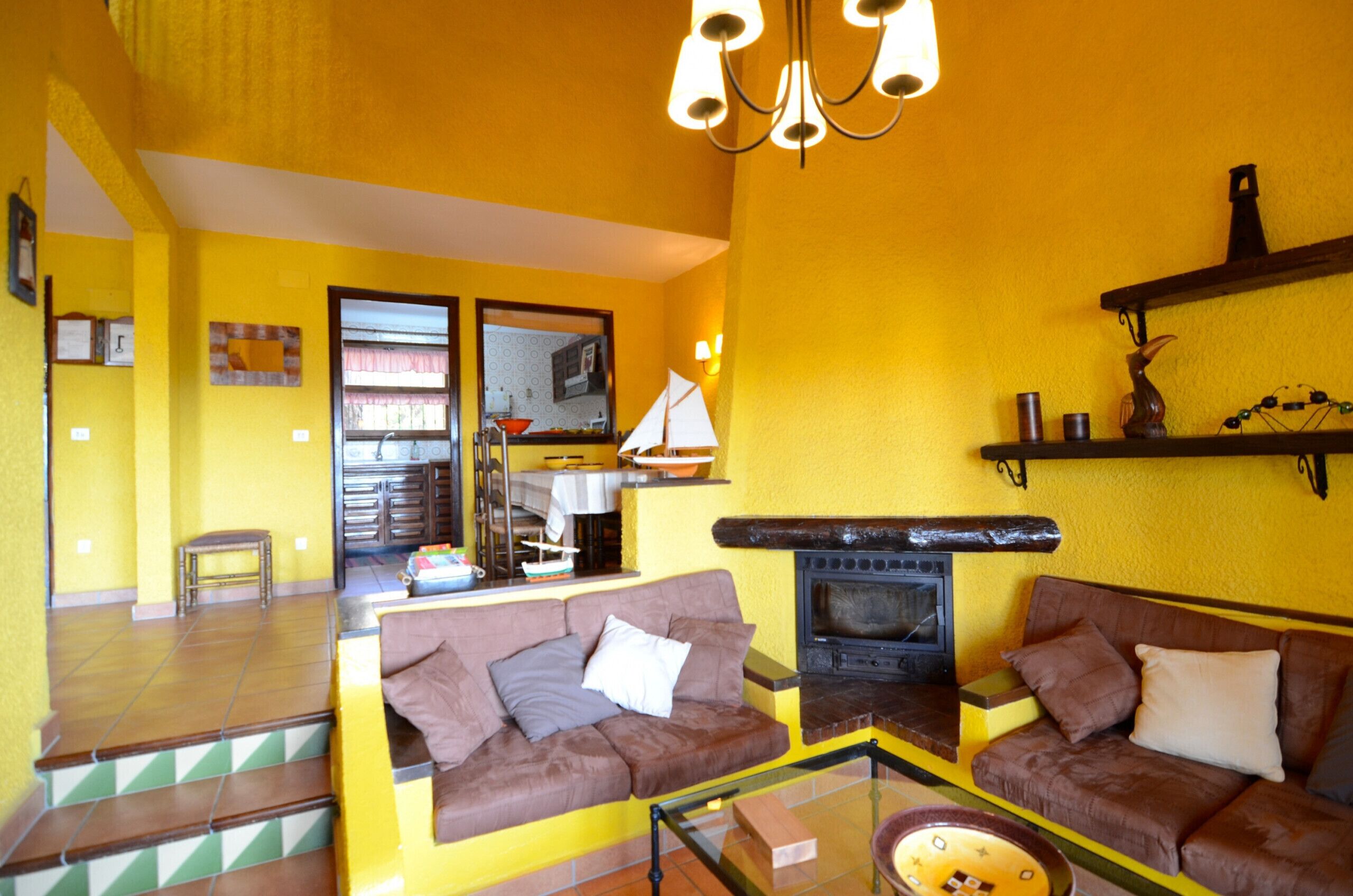 A living room with two sofas, a glass coffee table, a fireplace, and a kitchen visible through a glass door.