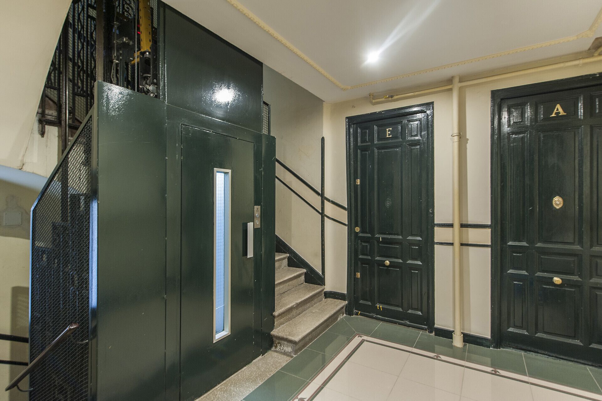 A staircase leading to a landing with two black doors, one marked with a gold 'A' and the other with a gold 'E'.
