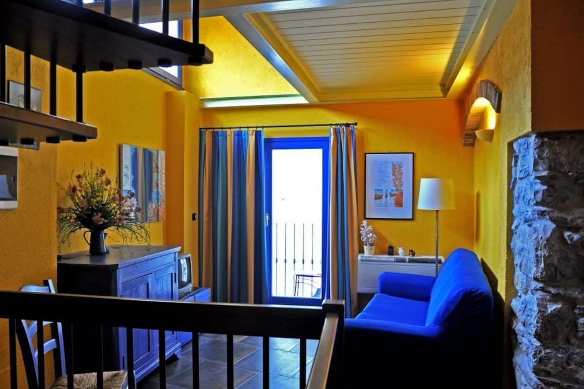 A room with a blue sofa, a small table with a vase, a staircase, and a view of the outside.
