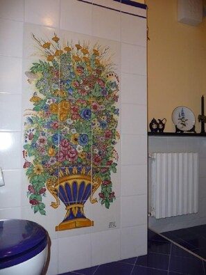 A bathroom with a decorative floral tile mural, a white radiator, and a blue-tiled floor. - Agriturismo Ca' dei Conti (San Bartolomeo al Mare)