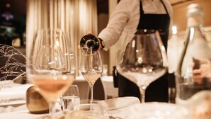 A dining table with wine glasses, a bottle, and a waiter pouring wine. - Garden Rooms (Maribor)