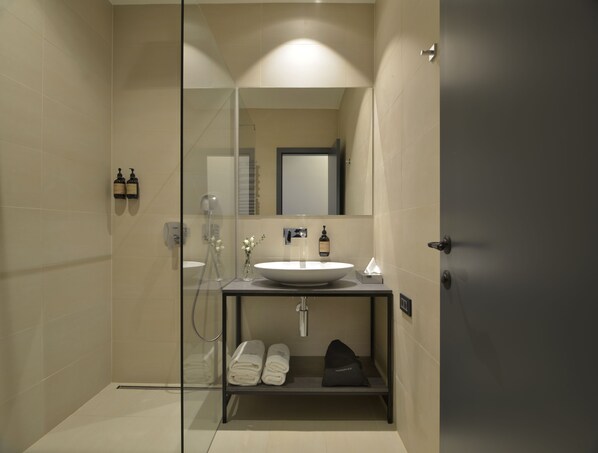 Un baño moderno con cabina de ducha de vidrio, un lavamanos con espejo y un perchero con toallas dobladas con cuidado.