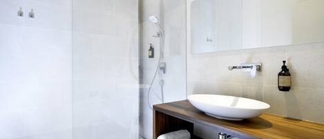 Un baño moderno con un lavamanos grande de color blanco, un mueble de tocador de madera, una mampara de ducha de vidrio y un espejo grande.