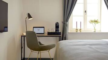Habitación de hotel con cama, escritorio con computadora, silla, lámpara y ventana con cortinas.