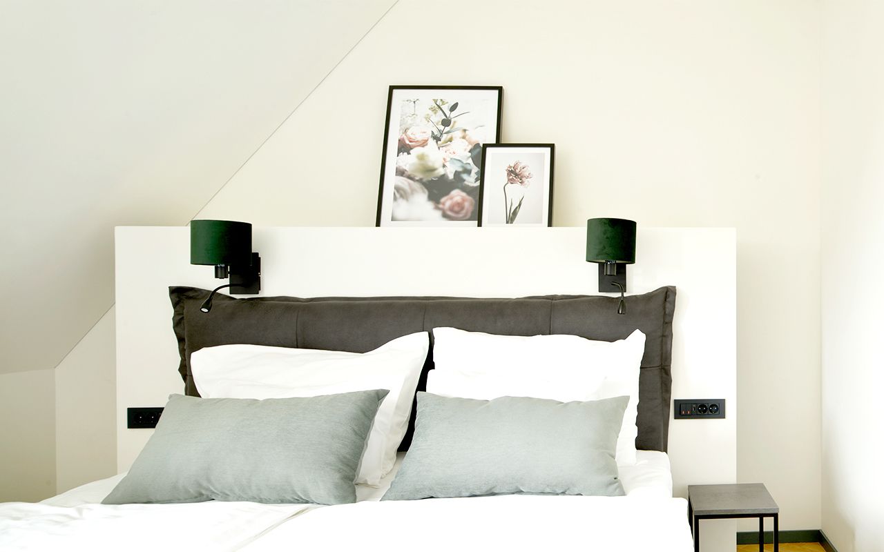 A modern bedroom with a large bed, two wall-mounted lamps, and framed artwork above the bed.